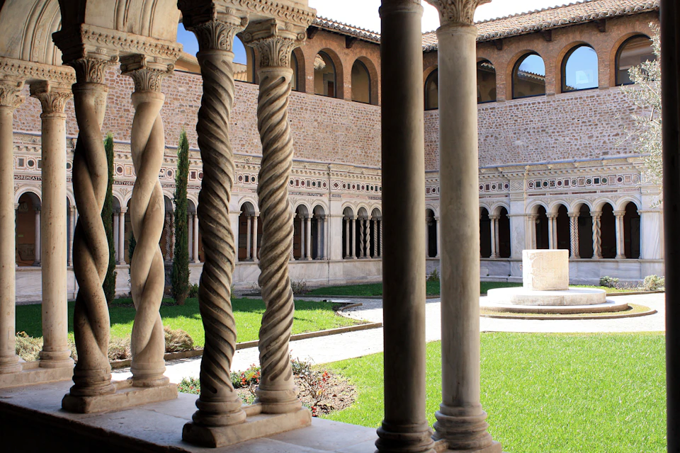 A courtyard with a grassy area, surrounded by arched columns and walls, viewed through intricately carved stone pillars.