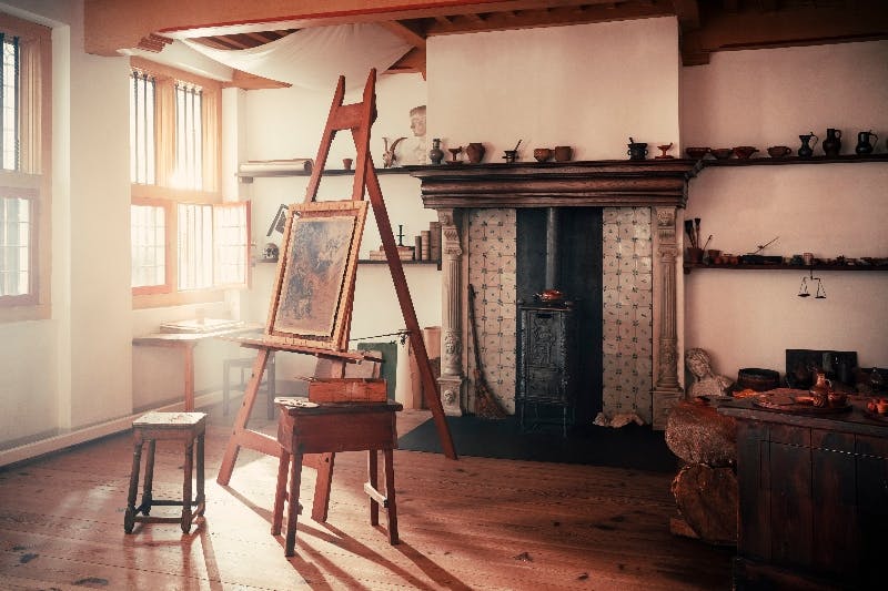 Ein rustikales Künstleratelier mit einer hölzernen Staffelei, einem Gemälde, einem Kamin und natürlichem Licht, das durch die Fenster strömt.