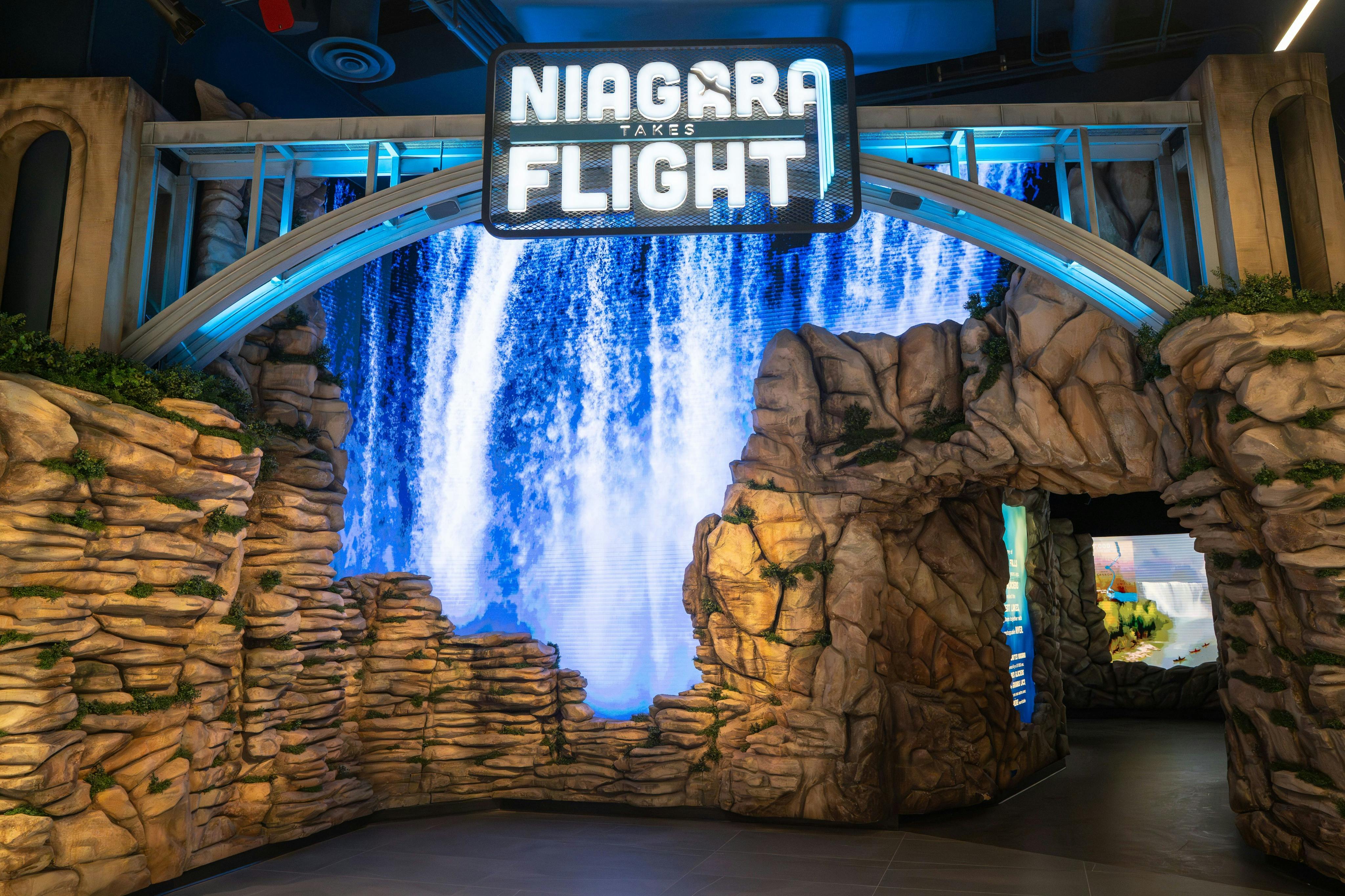 「Niagara Takes Flight」的入口标志以瀑布和岩层为背景，蓝色灯光照亮。
