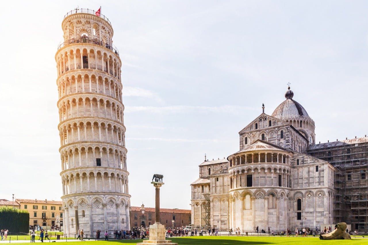 Ο κεκλιμένος πύργος της Πίζας και ο καθεδρικός ναός της Πίζας με τουρίστες σε ένα καταπράσινο γκαζόν κάτω από έναν καθαρό ουρανό.