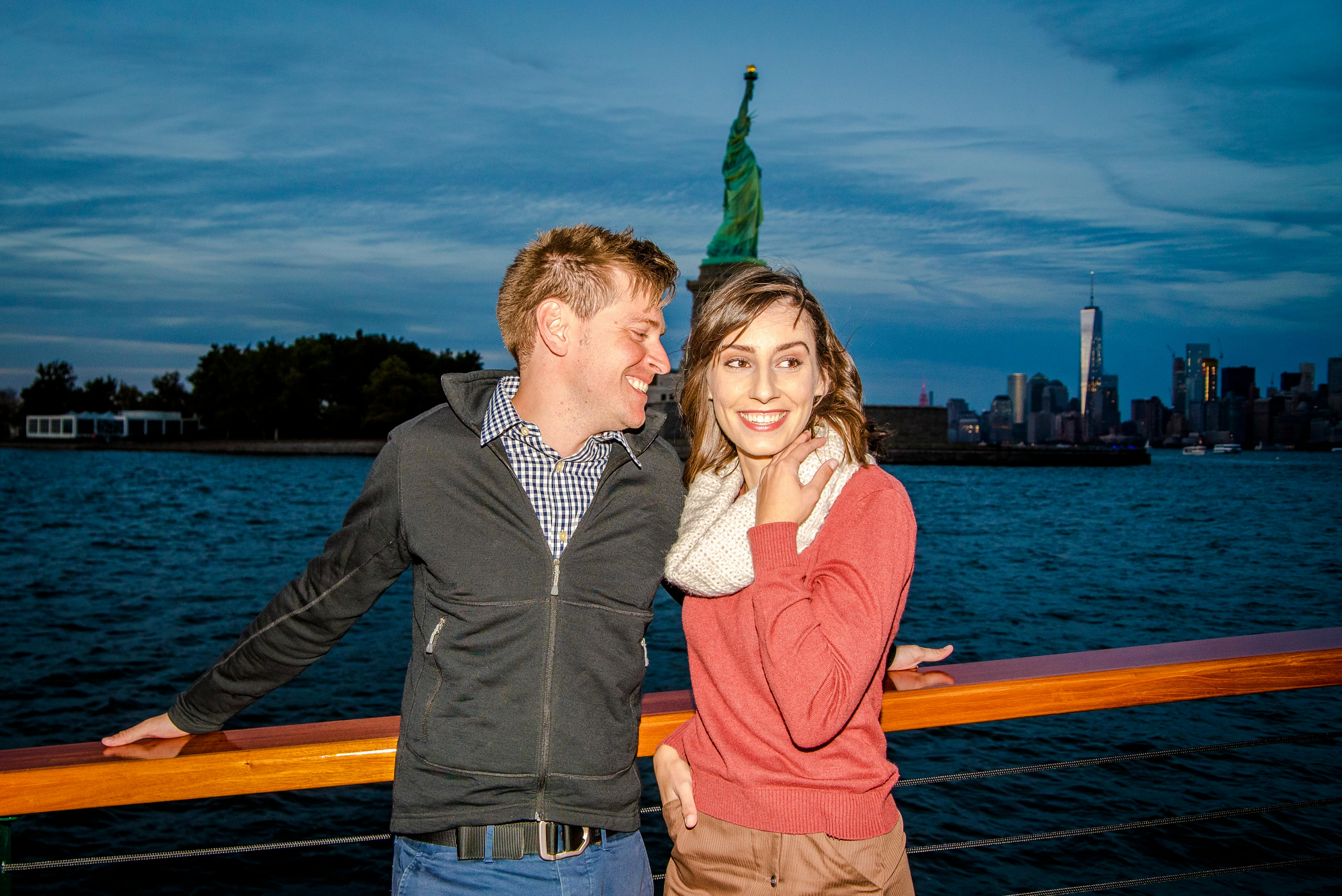 Ένα ζευγάρι χαμογελάει σε μια βάρκα με φόντο το Άγαλμα της Ελευθερίας και τον ορίζοντα της Νέας Υόρκης.