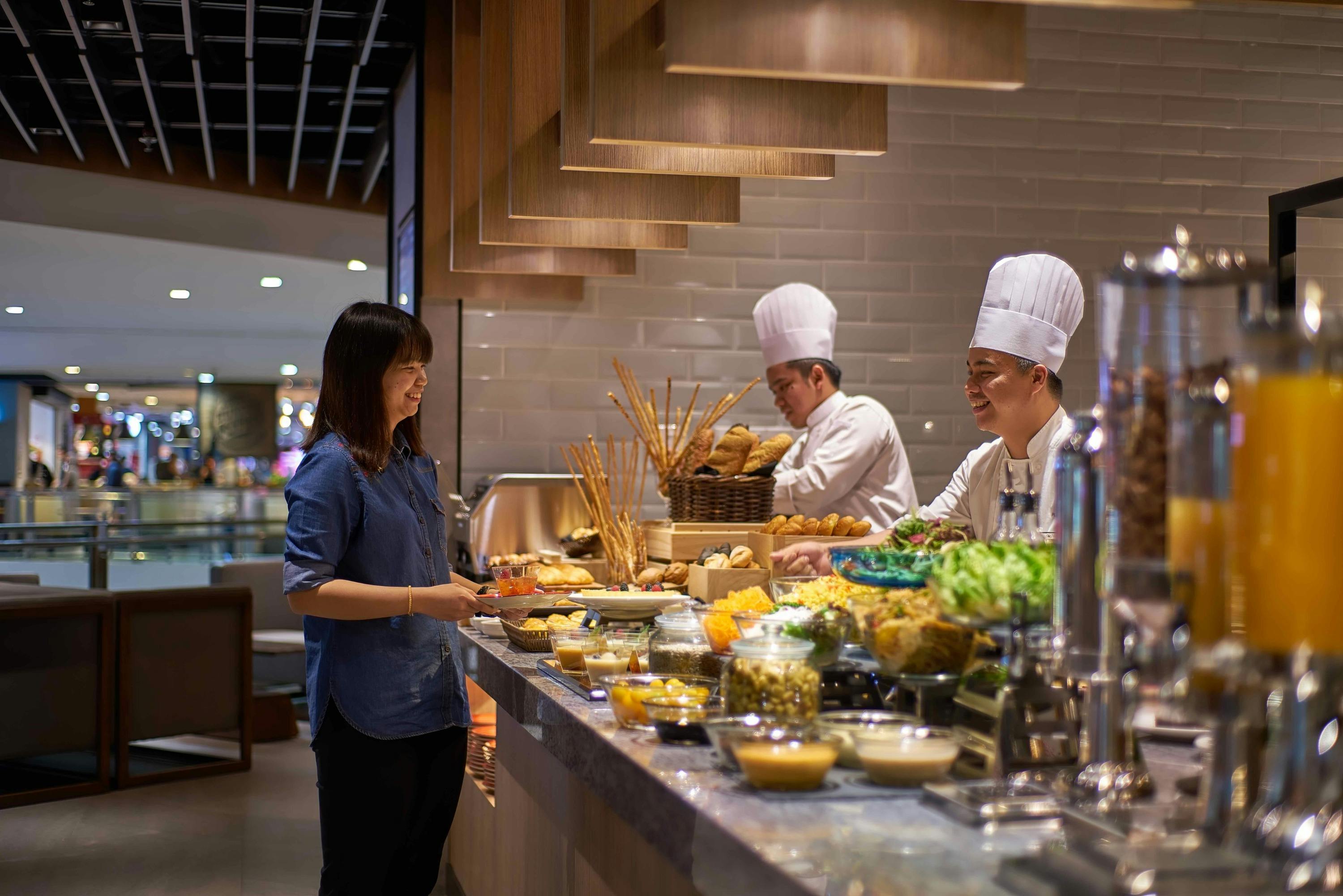 Chefs wearing white uniforms and hats prepare food behind a buffet counter with various dishes and drinks displayed.