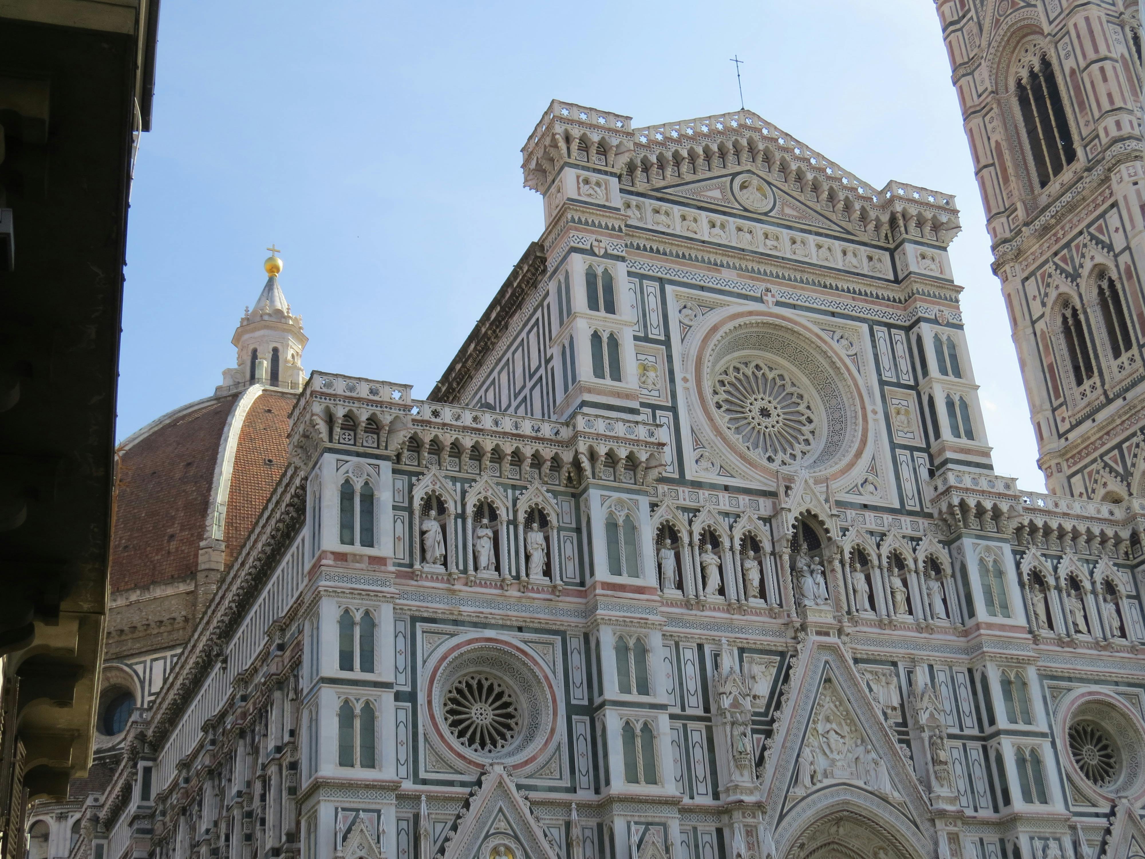 这座历史悠久的大教堂立面装饰华丽，设计精美，有拱门，背景中有一个大型圆顶。