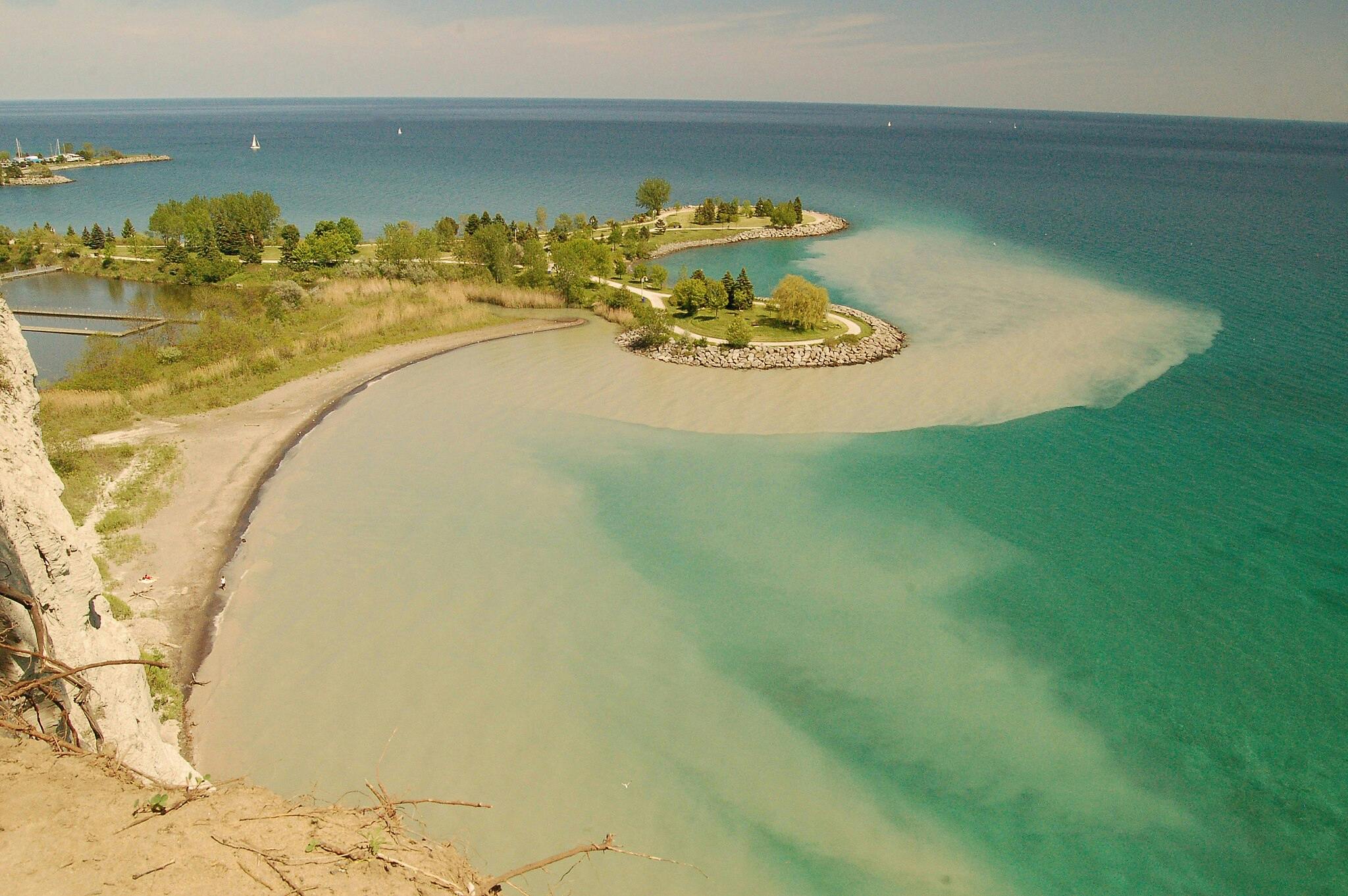 沙滩和清澈的绿松石水域，岩石海岸线和绿树成荫的公园延伸到湖中。