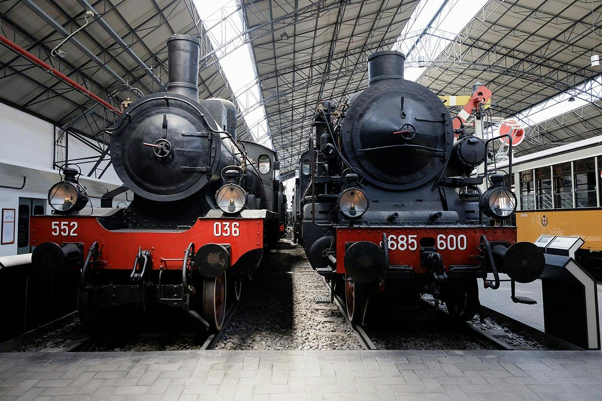 Due locomotive a vapore d'epoca esposte una accanto all'altra in una stazione ferroviaria con una copertura metallica sopra la testa.