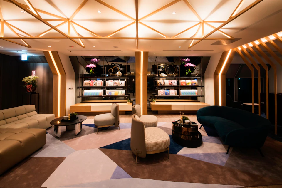A stylish lounge area with modern furniture, geometric lighting, and shelves displaying books and decor.