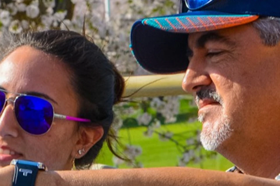 A man and a woman sitting on a double-decker bus, looking at a map, with blooming trees and a park in the background.