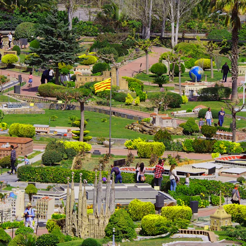 Människor som går genom en park med miniatyrmodeller av kända byggnader, frodig grönska och en liten damm.