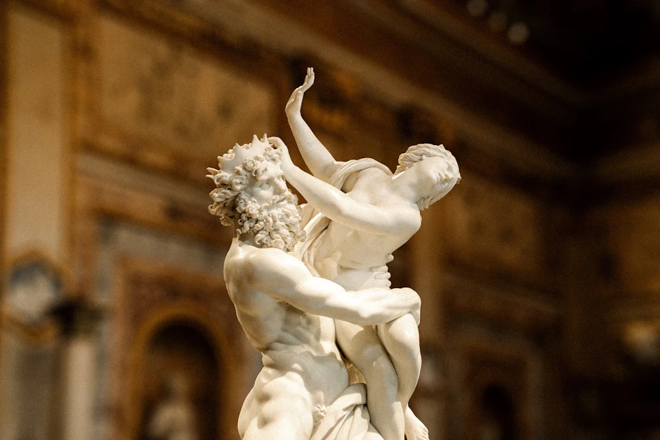 A marble statue depicting two figures in a dynamic pose, displayed in an ornate indoor setting.