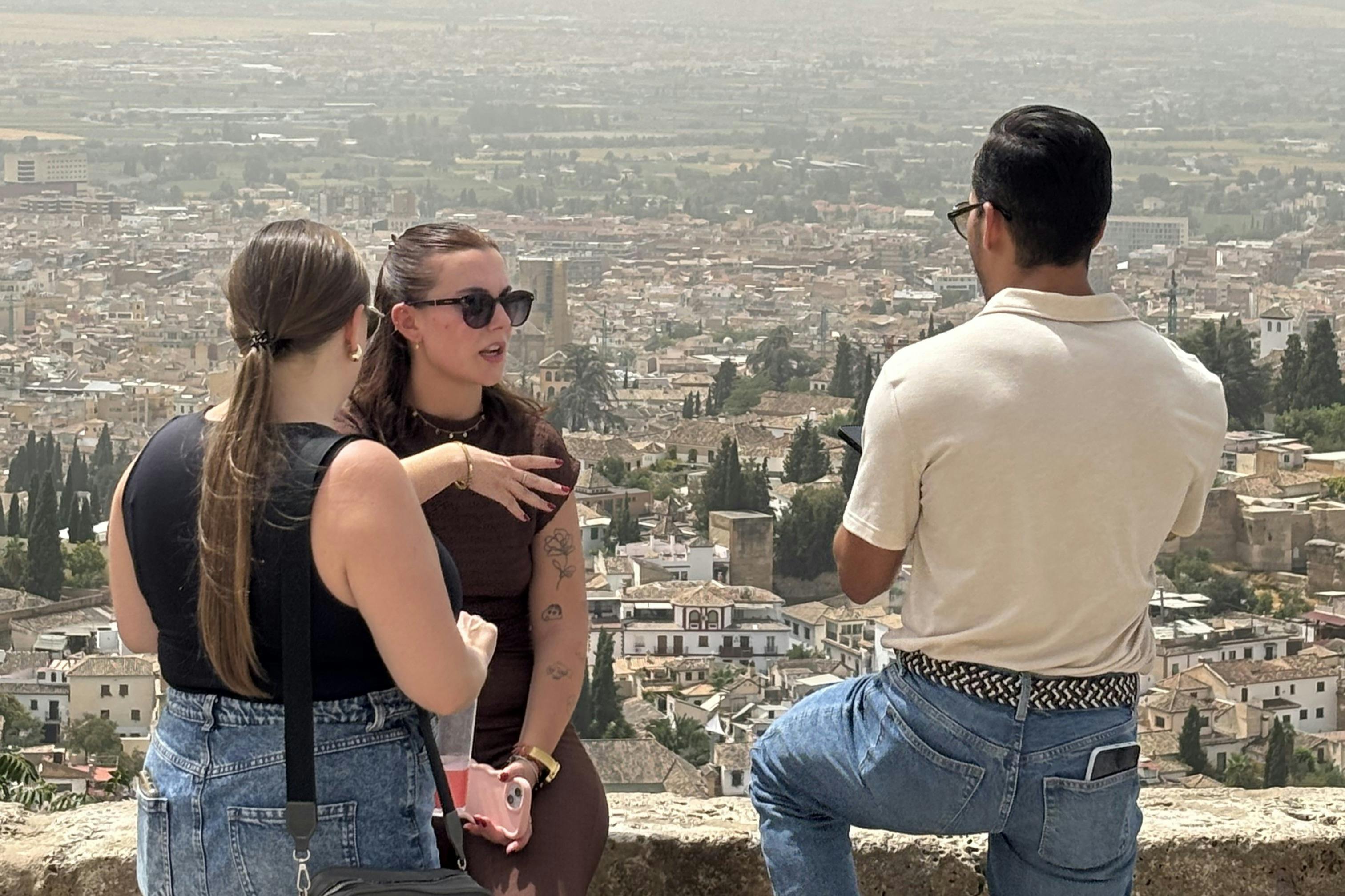 两个女人在城市前面聊天，一个戴着太阳镜，另一个背着背包。 背景是一座城市的屋顶景观。