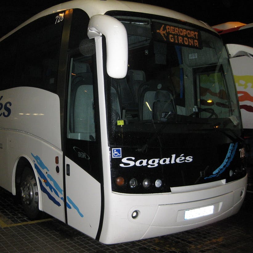 White Sagales bus with a "Aeroport Girona" sign on the front display, parked at a bus terminal.