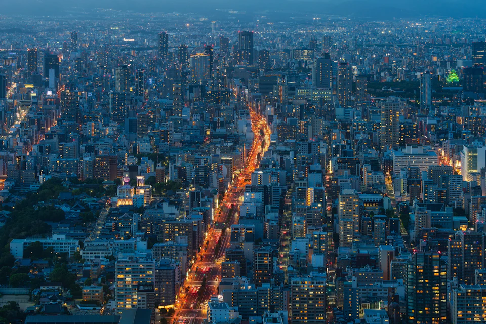 Aerial view of a cityscape with illuminated streets and dense high-rise buildings at dusk.