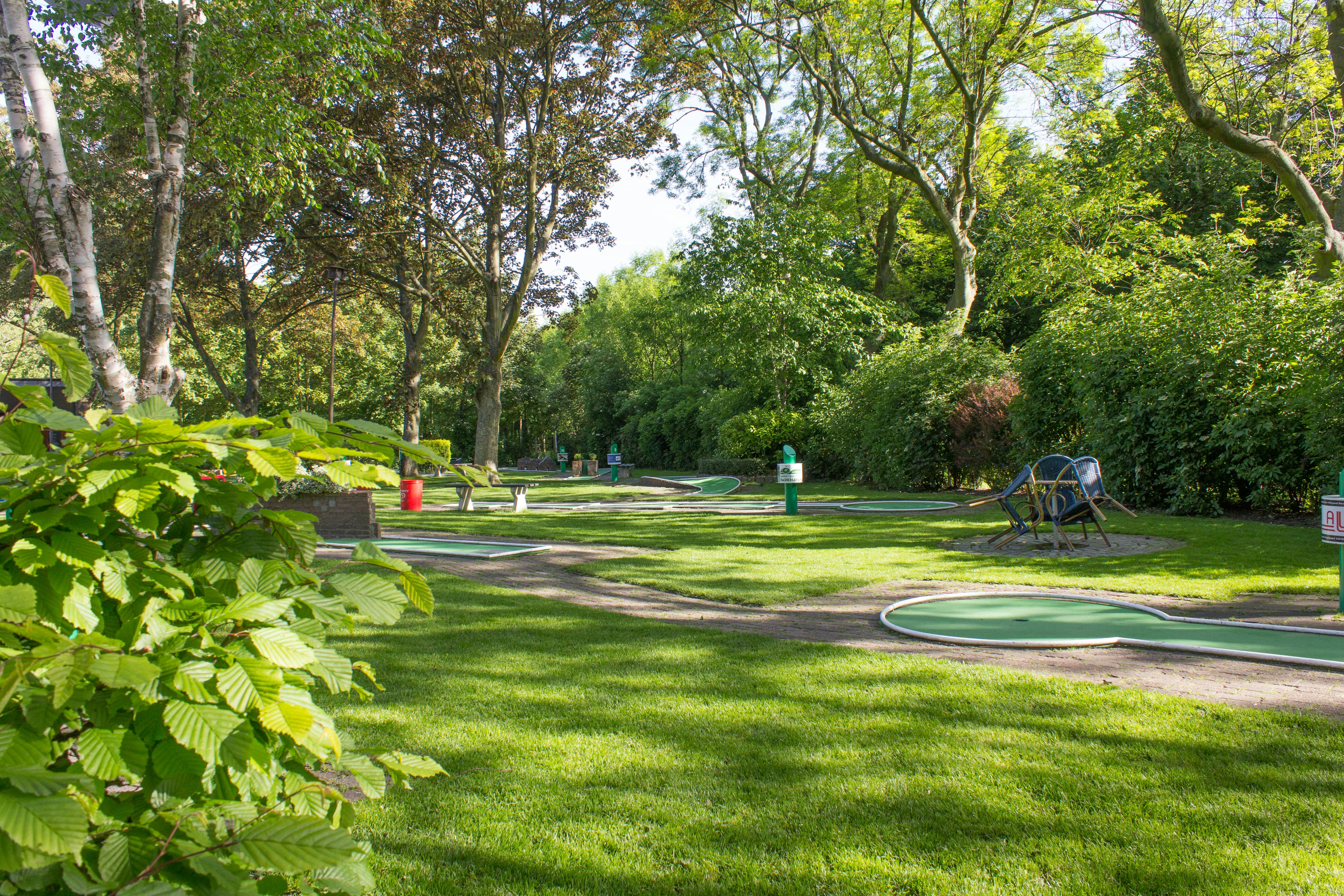 园景迷你高尔夫球场，绿地绿意盎然，四周环绕着树木、草地和长凳。