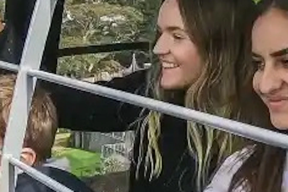 Four people inside a cable car, looking out through the metal bars at green scenery below on a sunny day.