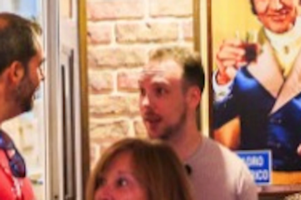 A group of people conversing inside a cozy, decorated room with hanging items and shelves of bottles under warm lighting.