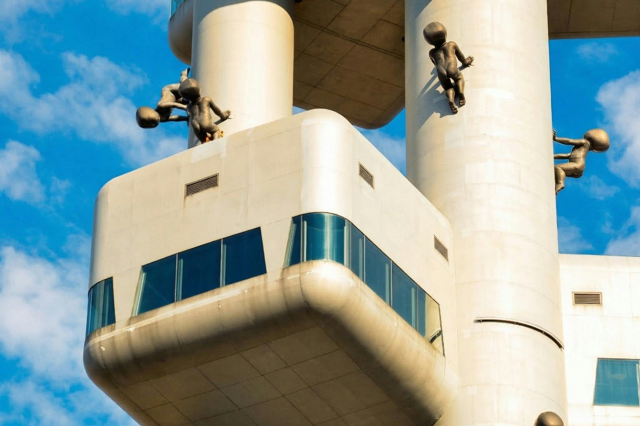 Une tour moderne avec des terrasses d'observation vitrées et des sculptures d'enfants rampants attachées à sa surface.