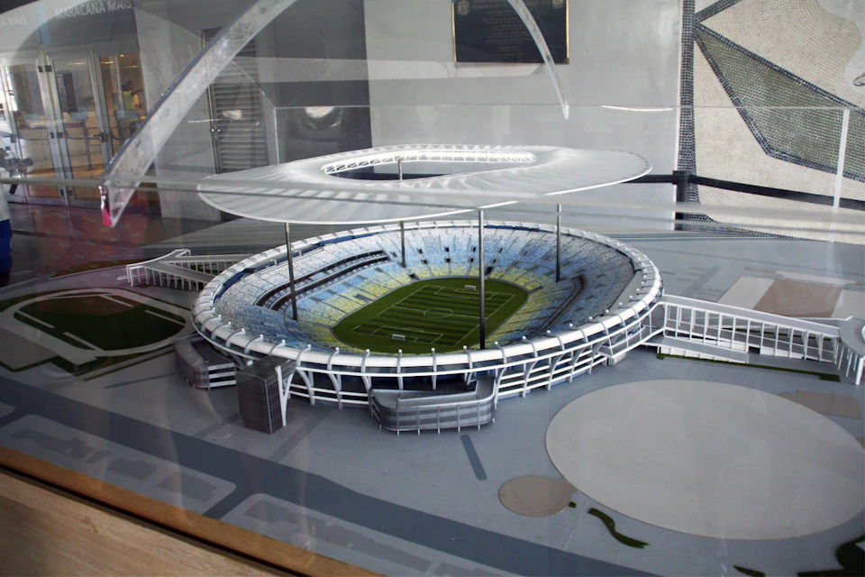 A scale model of a modern stadium with a circular design, tiered seating, and a large canopy.