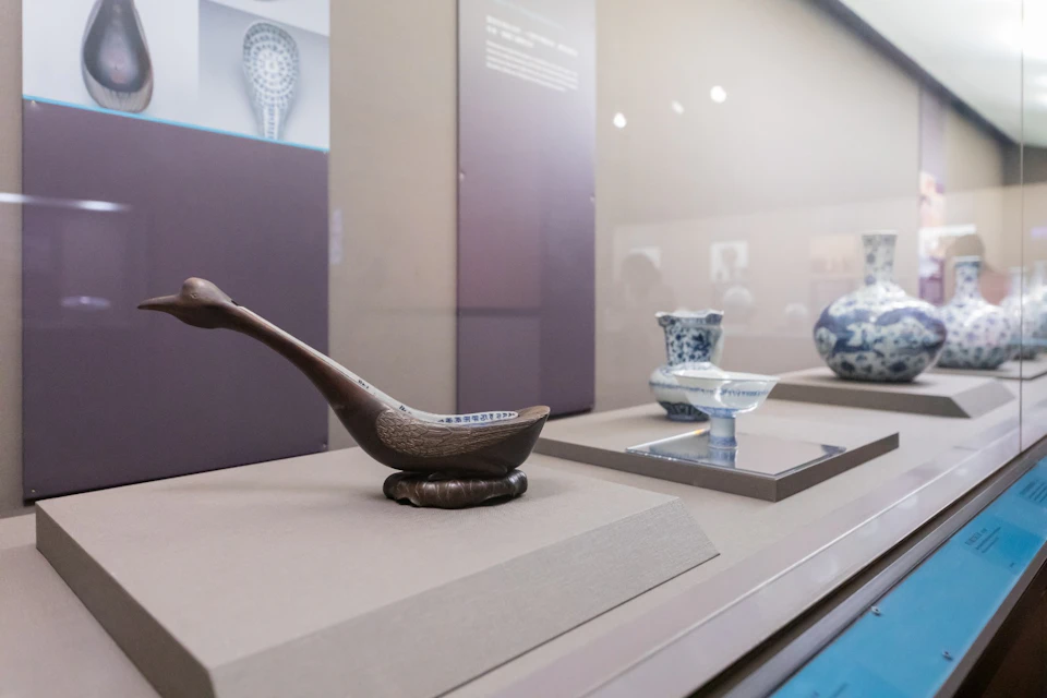 Exhibit of historical ceramic artifacts displayed in a museum showcase, including bowls and a ladle on a beige platform.