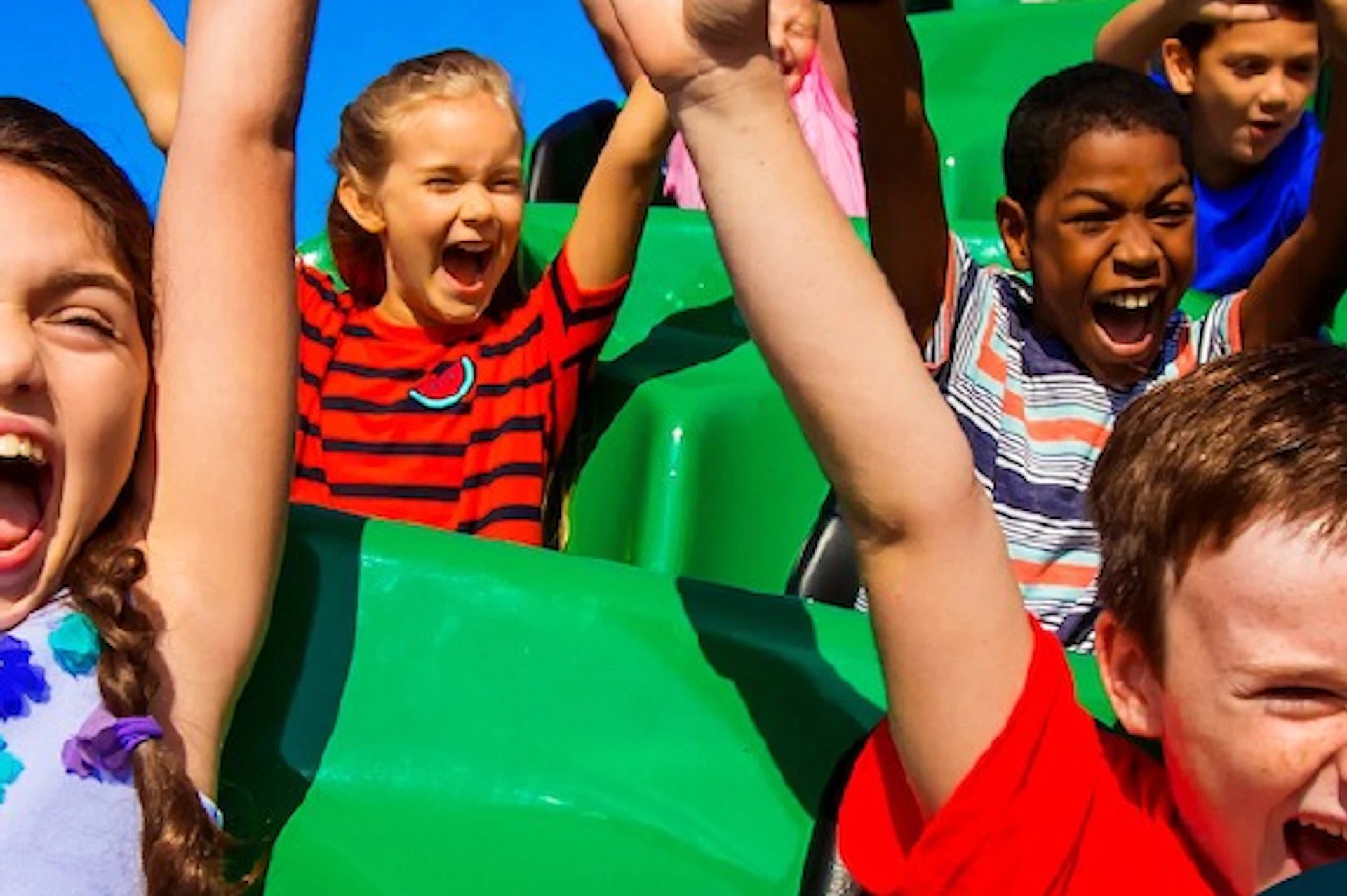 Children riding a roller coaster, with a digital pass for Go City Orlando displayed in the foreground.