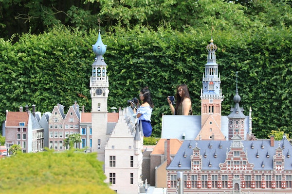 Dos personas fotografiando miniaturas arquitectónicas detalladas sobre un fondo de exuberante vegetación.