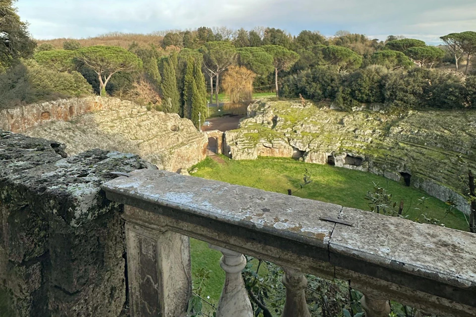 A view of a stone balustrade overlooking a verdant landscape with rock formations, trees, and a pathway under a cloudy sky.