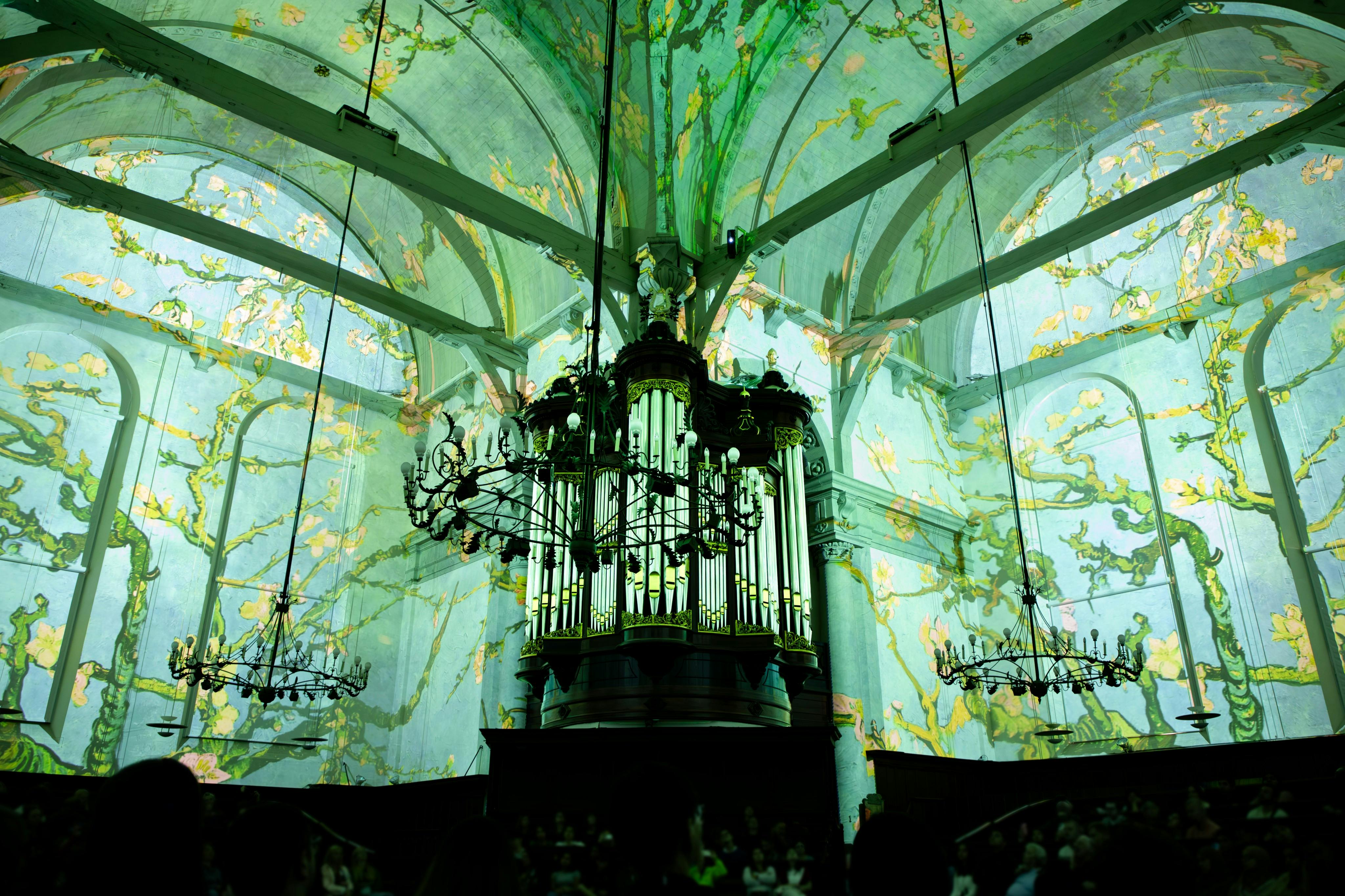 大きなシャンデリアがあり、中央にパイプオルガンがあり、アーチ型の天井を覆っている緑と黄色の壁画がある大聖堂。