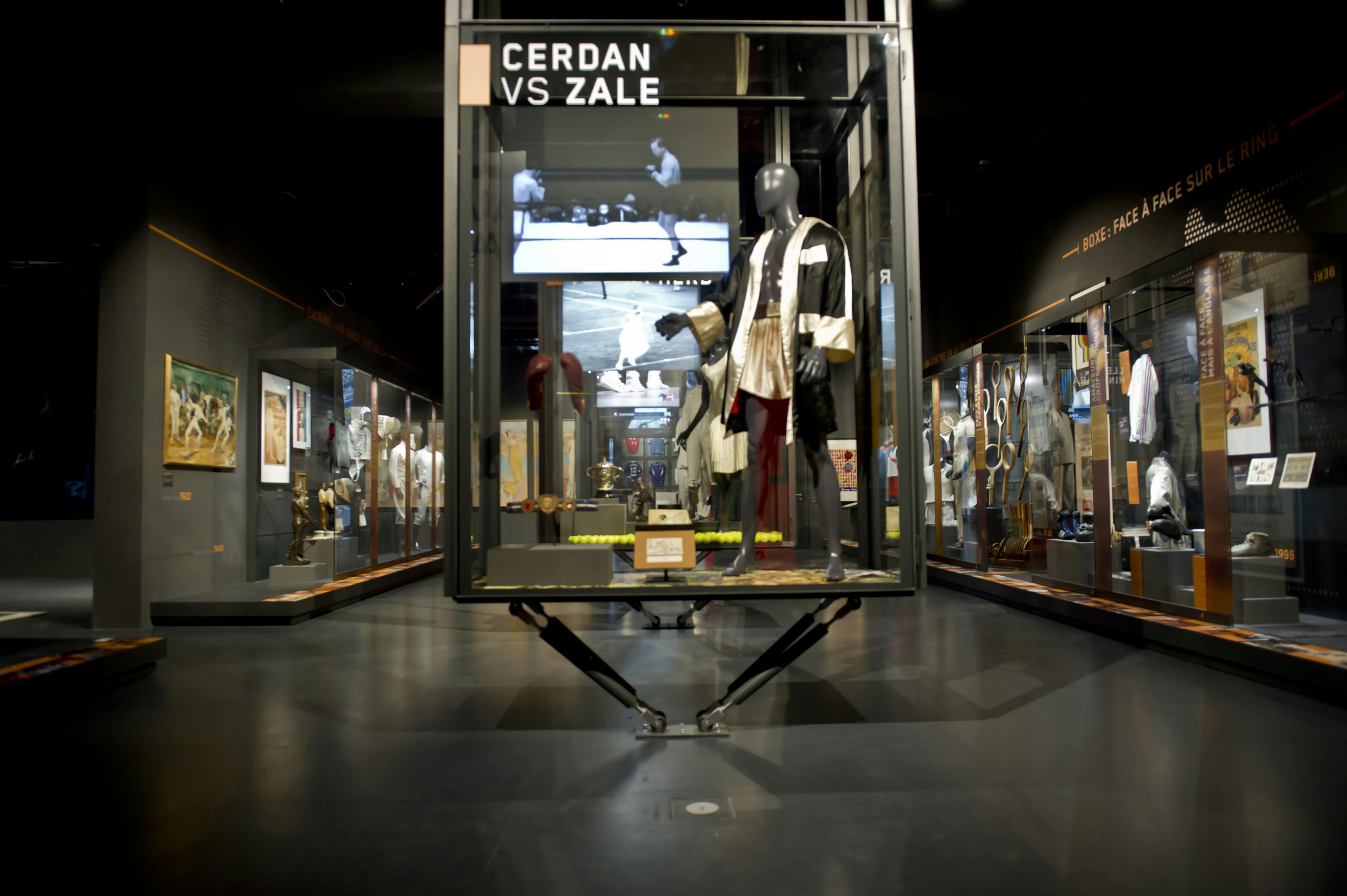 Expozice muzea s vitrínou s boxerskými suvenýry, včetně županu na figuríně a nápisem „Cerdan vs Zale“.