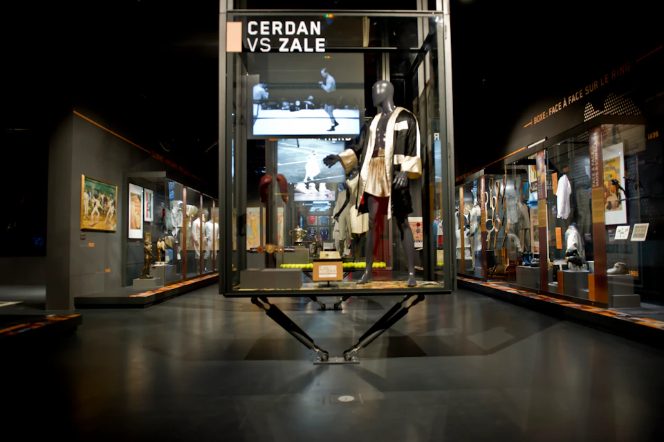 Museum exhibit featuring a display case with boxing memorabilia, including a robe on a mannequin and the text "Cerdan vs Zale."