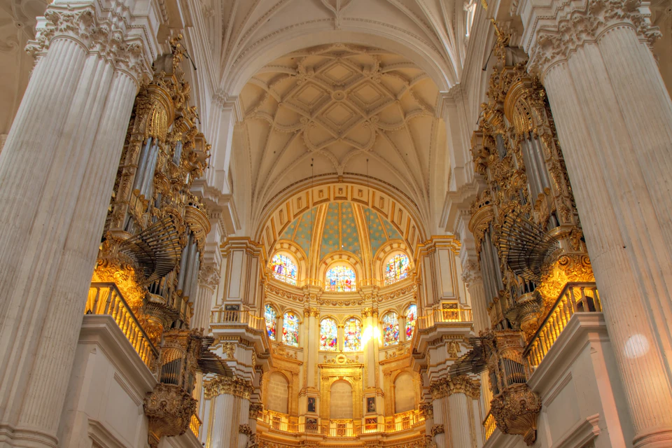 Interior of a grand cathedral with ornate golden details, stained glass windows, and a vaulted ceiling.