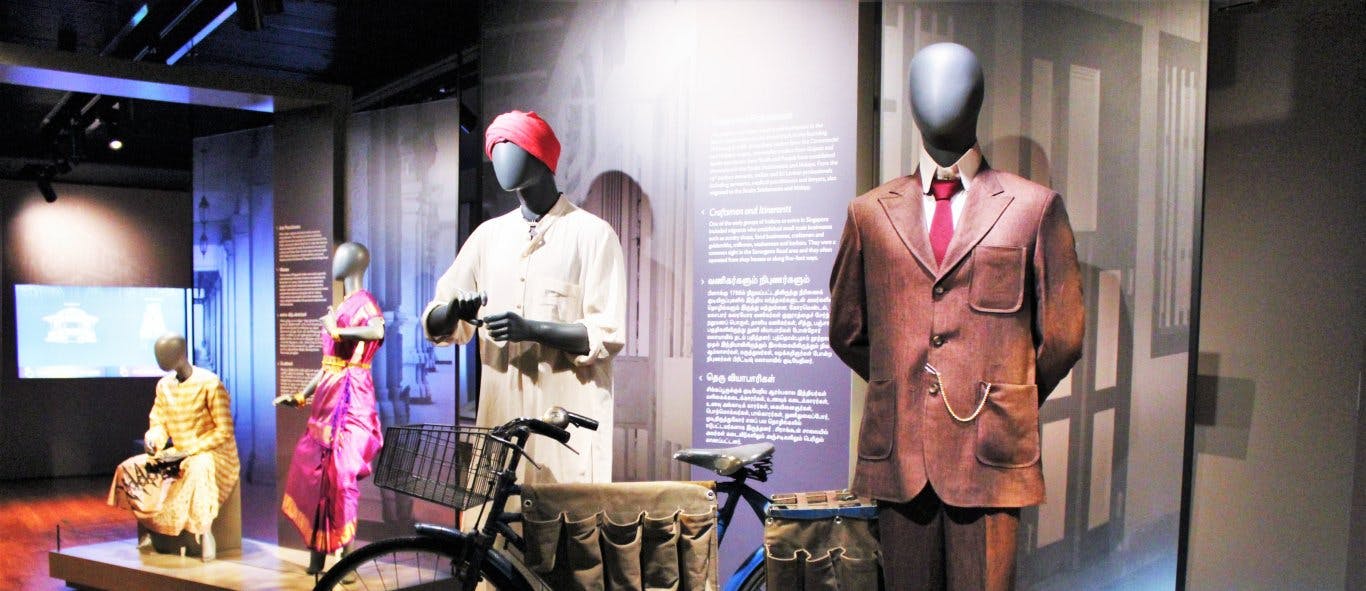 Манекены, одетые в традиционную и официальную одежду, рядом с велосипедом с панье в музейной экспозиции.