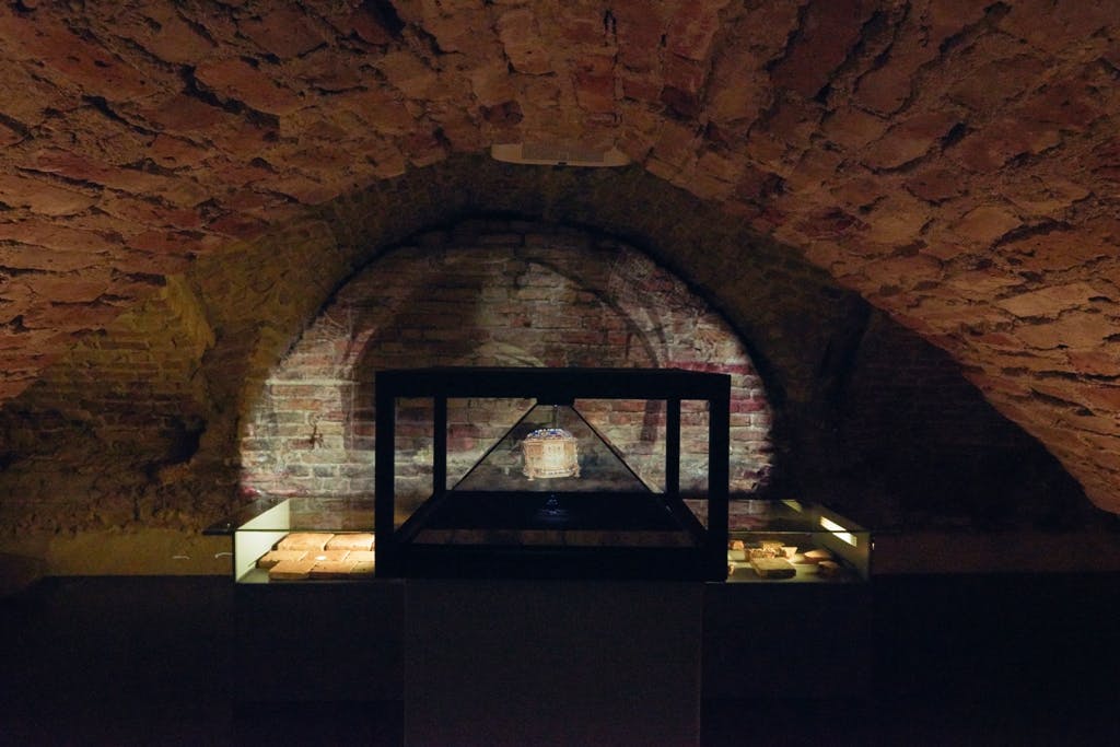 灯光昏暗的砖墙房间，带有带照明的展示柜，里面放着一件神器，两侧是带照明的架子。