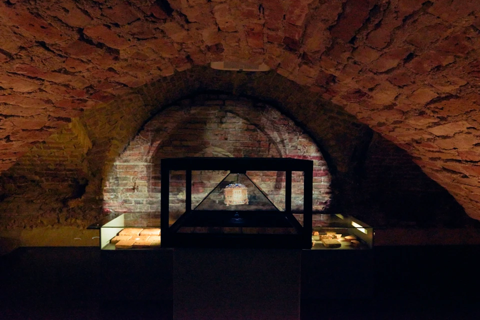 Dimly lit brick-walled room with an illuminated display case holding an artifact, flanked by illuminated shelves.