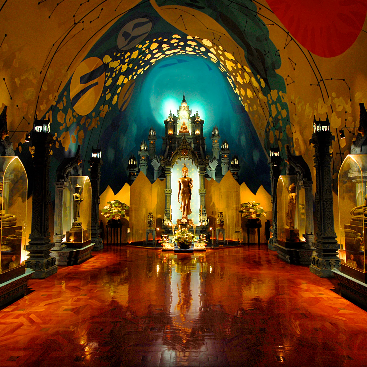Ornate hall with a high, painted ceiling, statues in glass cases, and a central golden figure surrounded by lights and flowers.