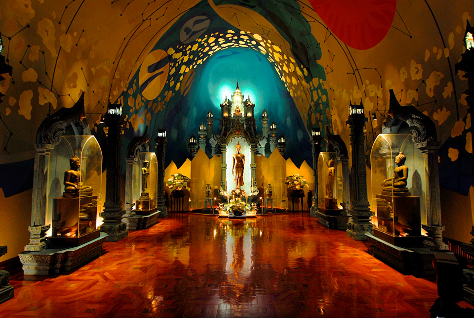 Ornate hall with a high, painted ceiling, statues in glass cases, and a central golden figure surrounded by lights and flowers.