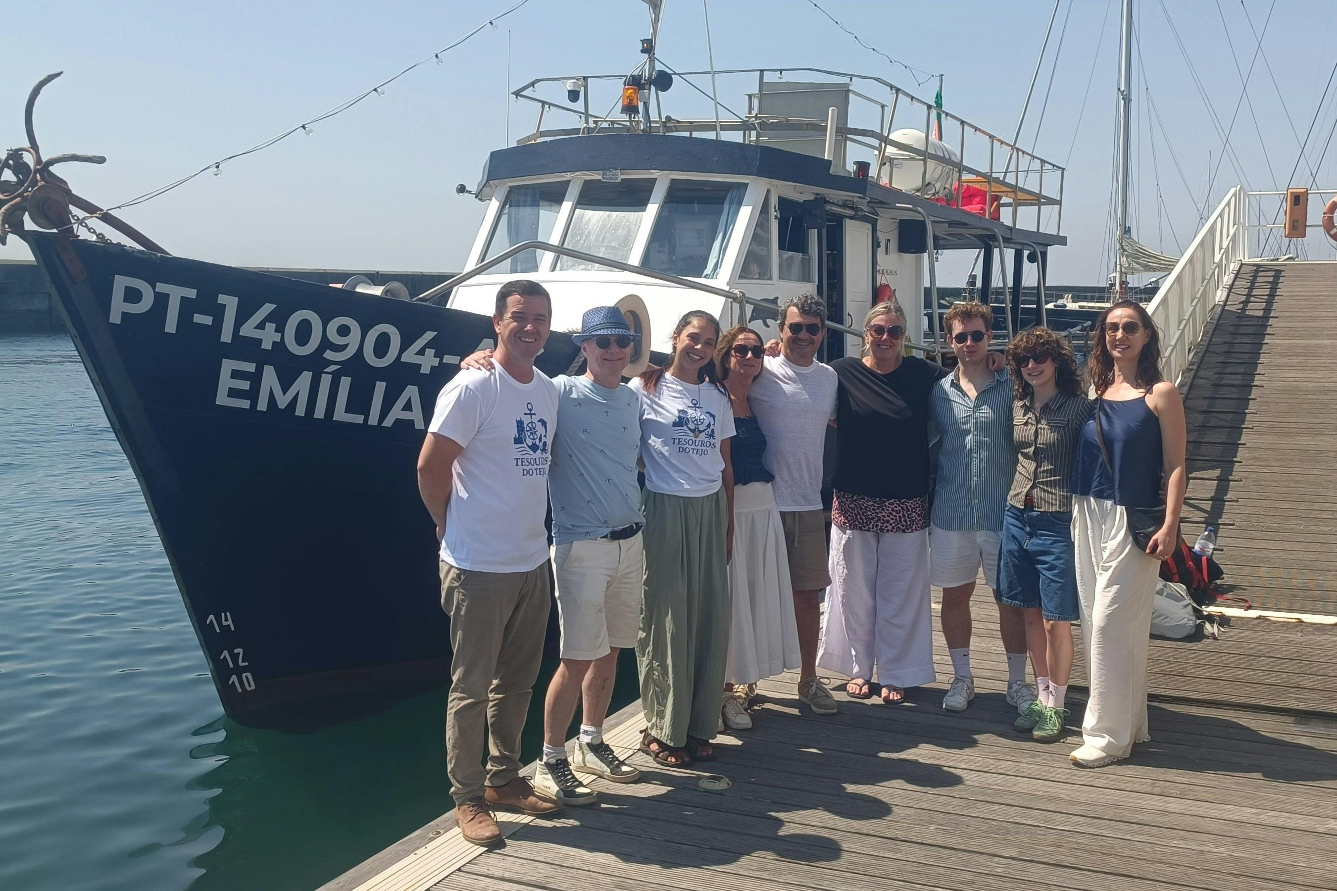 天気のいい日には、8人のグループがボートの前の波止場に立って笑顔でポーズをとって写真を撮っています。