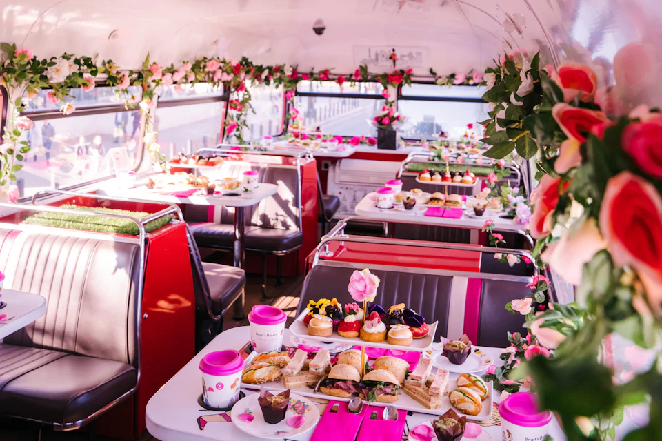 A decorated bus interior with floral arrangements and tables set with tea, pastries, and sandwiches for an afternoon tea.
