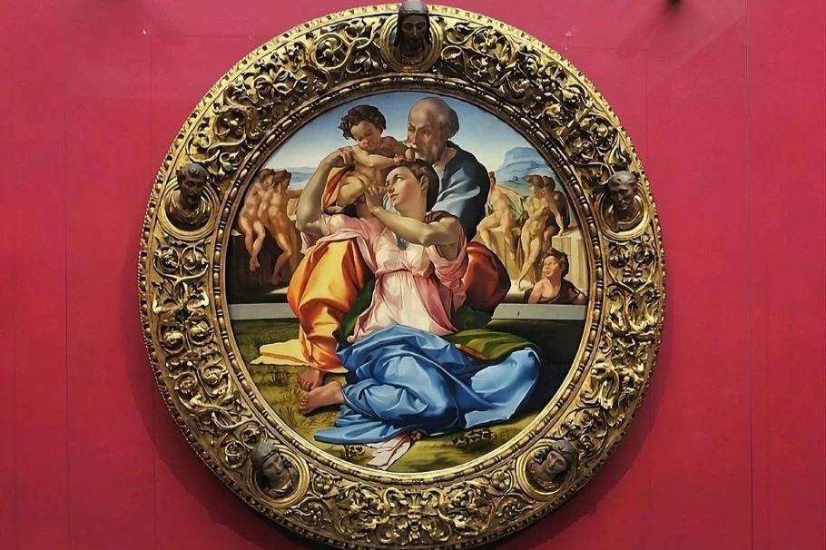 A circular painting depicts a family with an infant surrounded by elaborately carved golden frame, set against a red background.