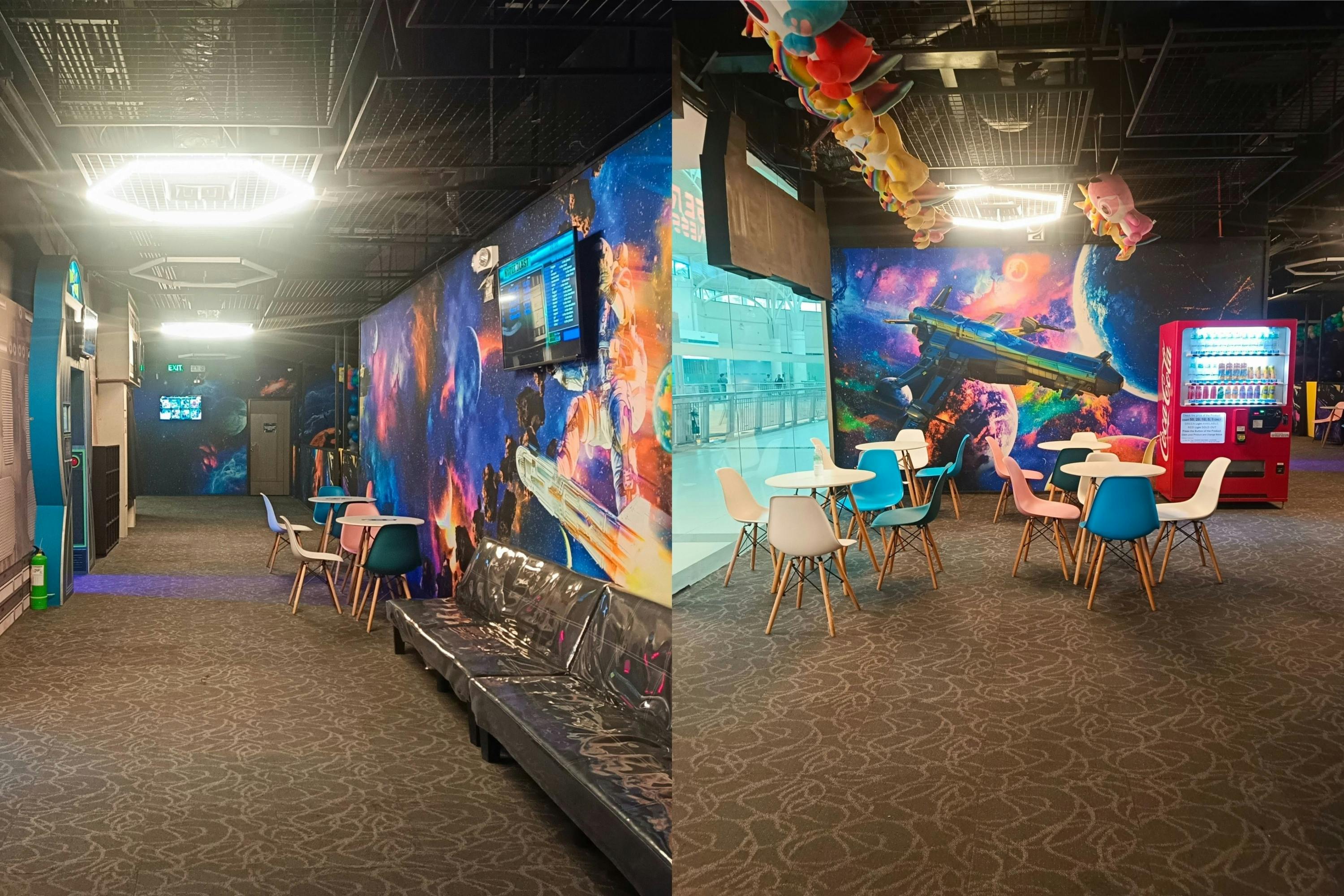 A colorful indoor seating area with space-themed wall art, chairs, tables, and a bench under bright ceiling lights.