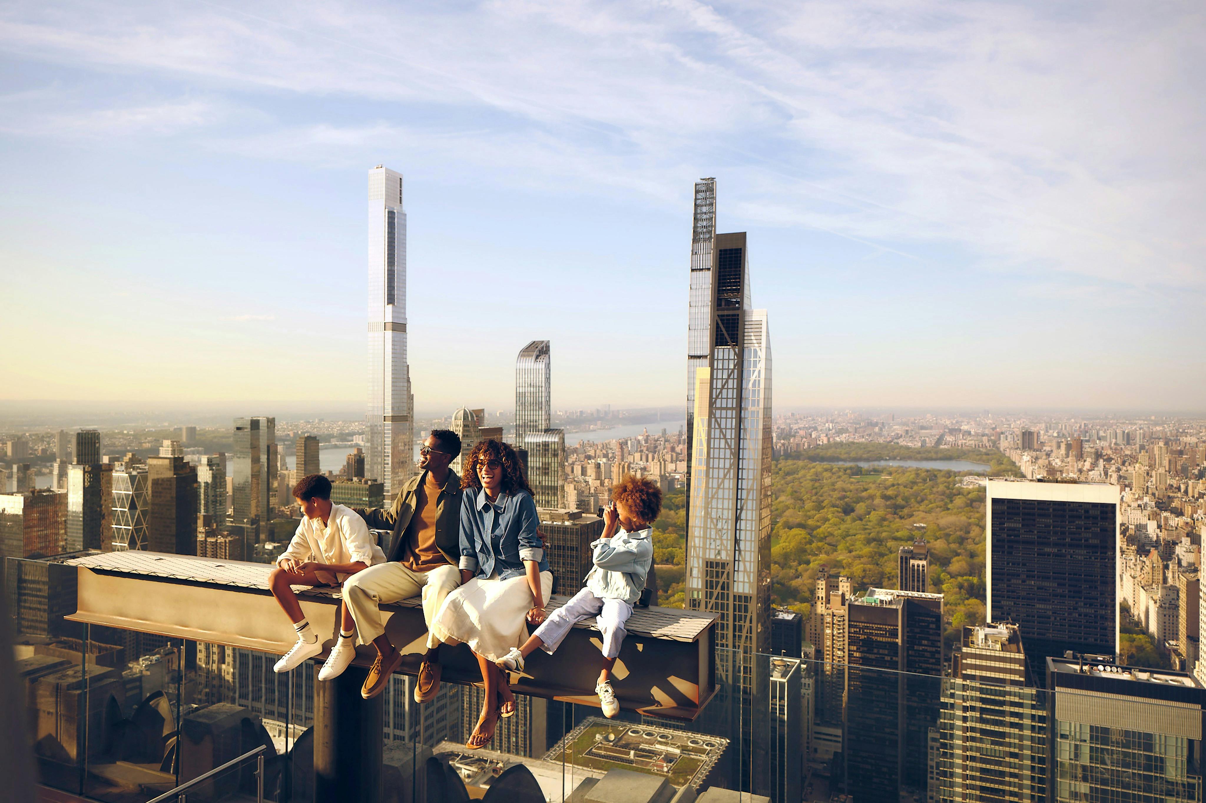 Un grup de quatre persones assegudes en una biga amb vistes a un paisatge urbà amb edificis alts i un parc.