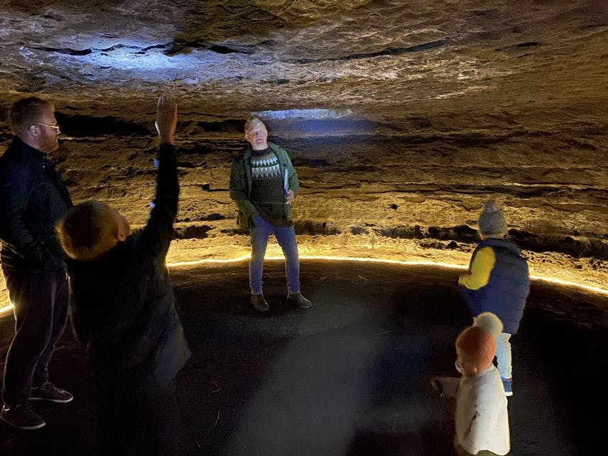 A group of people in a dimly lit cave, one person pointing at the ceiling while another appears to be speaking.
