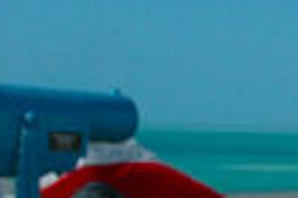 A boy rings a bell on a wooden deck overlooking the ocean, while a girl looks through a telescope. Red, white, and blue decorations are present.