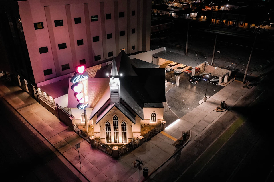 Aerial view of a building with stained glass windows, lit signs with hearts and text, and surrounding streets at night.