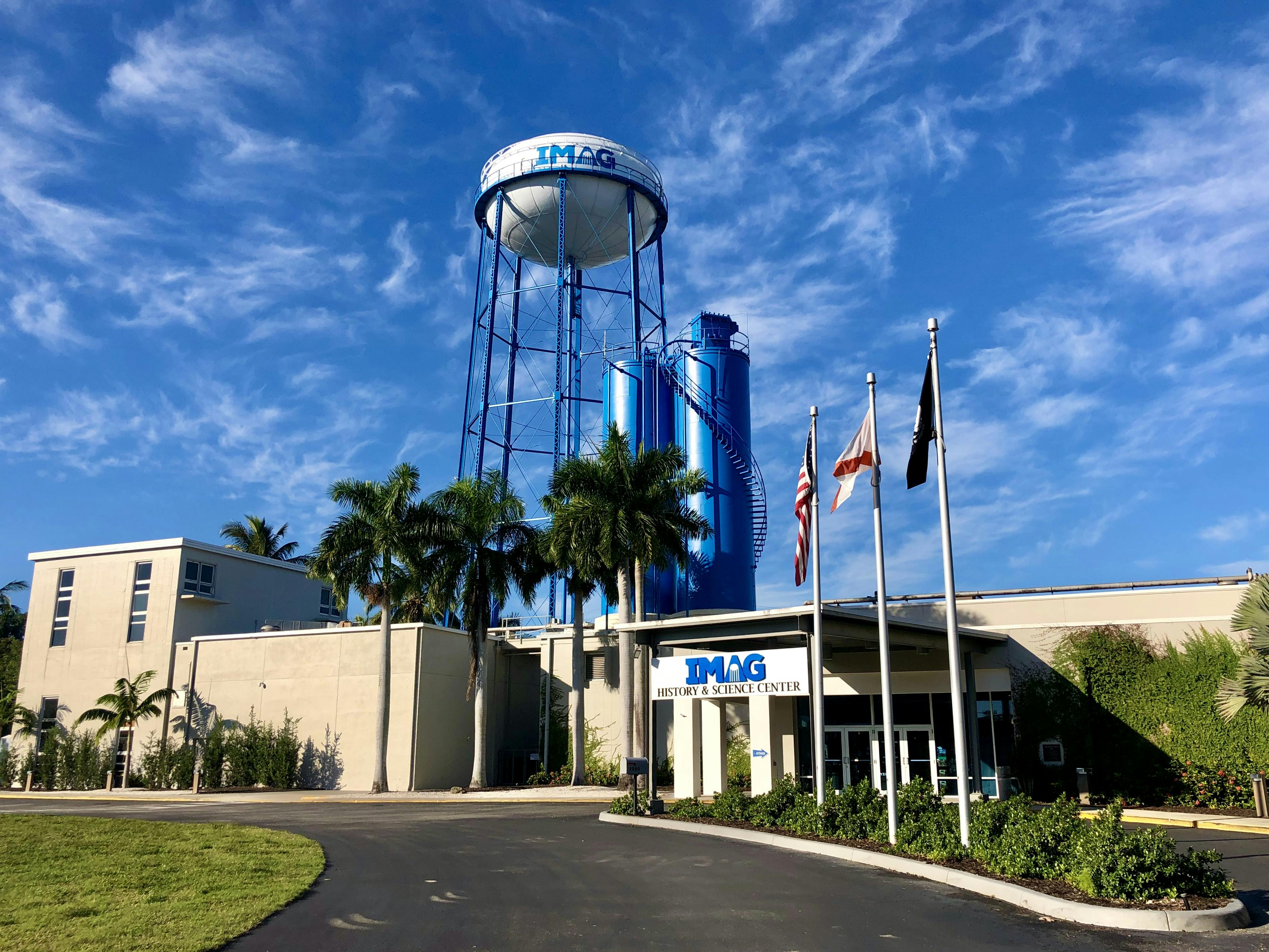 PŘEDSTAV si vstup do Centra historie a vědy s vlajkami, palmami a velkou modrou vodárenskou věží proti jasné obloze.