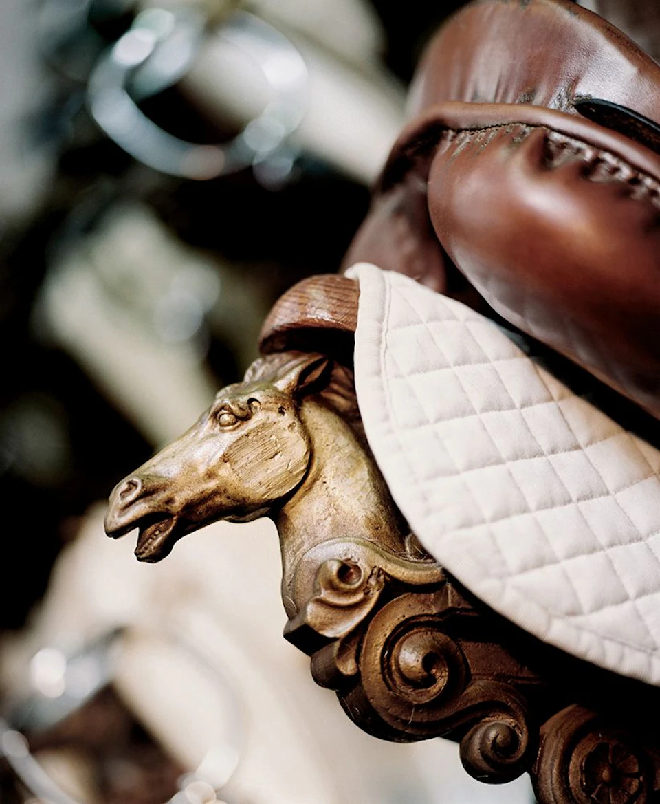 Close-up of a vintage carousel horse head, detailed in gold, beneath a brown leather saddle and a white quilted pad.