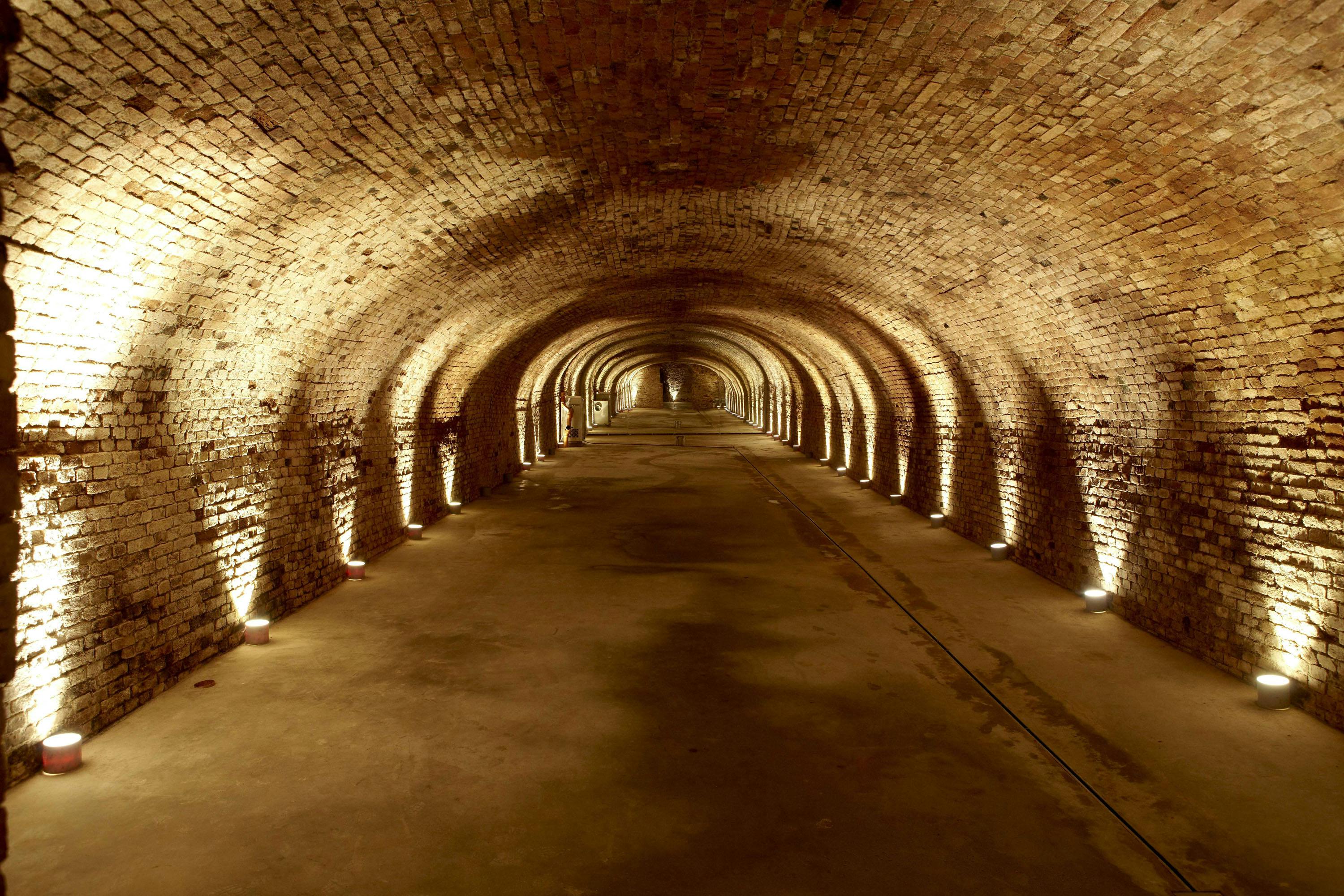 An empty, well-lit brick tunnel with a curved ceiling and arched walls, extending into the distance.