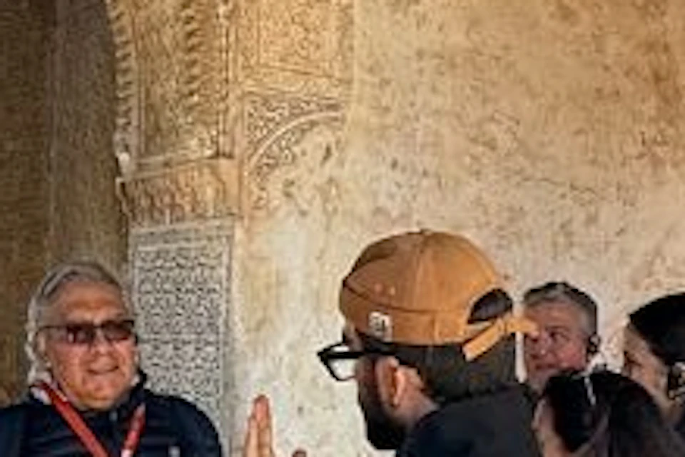 A group of people in a historical building with intricate carved archways and windows, some wearing tour guide headsets.
