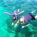 A father and child, continuing to snorkel, share a peaceful surface view while observing the underwater wonders together.