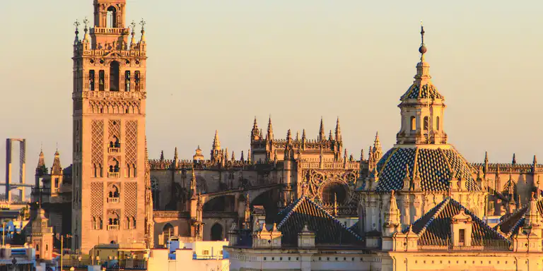Paysage urbain historique avec la tour Giralda et le dôme de la cathédrale de Séville au coucher du soleil, avec les toits au premier plan.