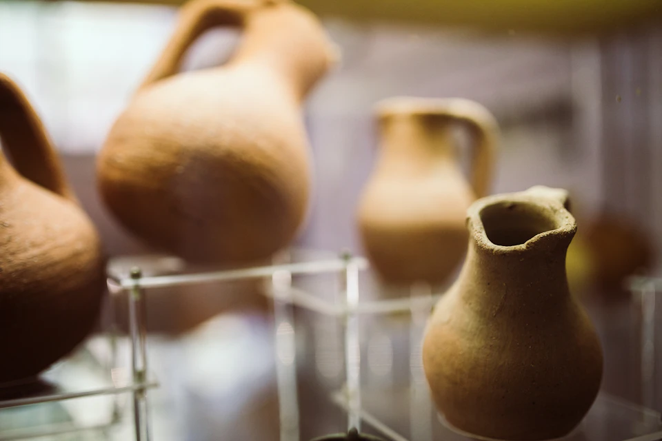 Three ancient clay jugs displayed on clear stands in a museum setting.