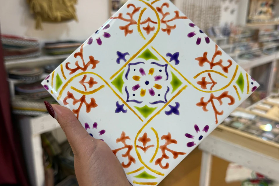 A decorative ceramic tile with colorful floral and geometric patterns, held by a person with painted nails.